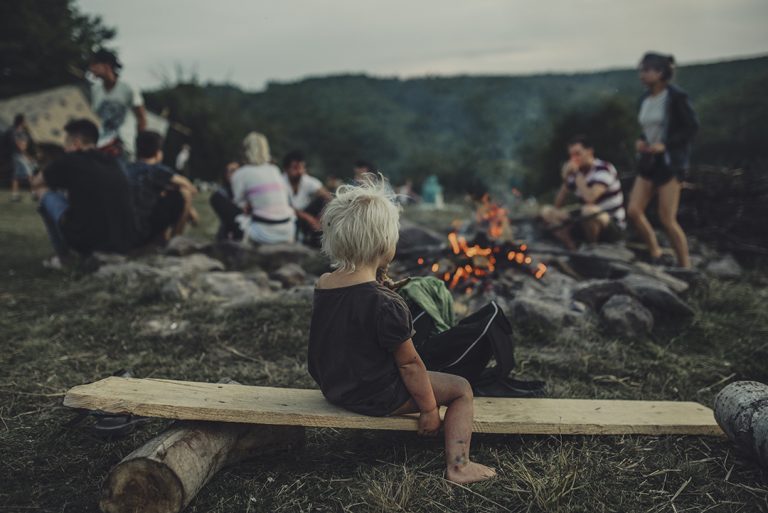 Copil pe o bancă în jurul focului de tabără, la Waha Festival Copil pe o bancă în jurul focului de tabără, la Waha Festival